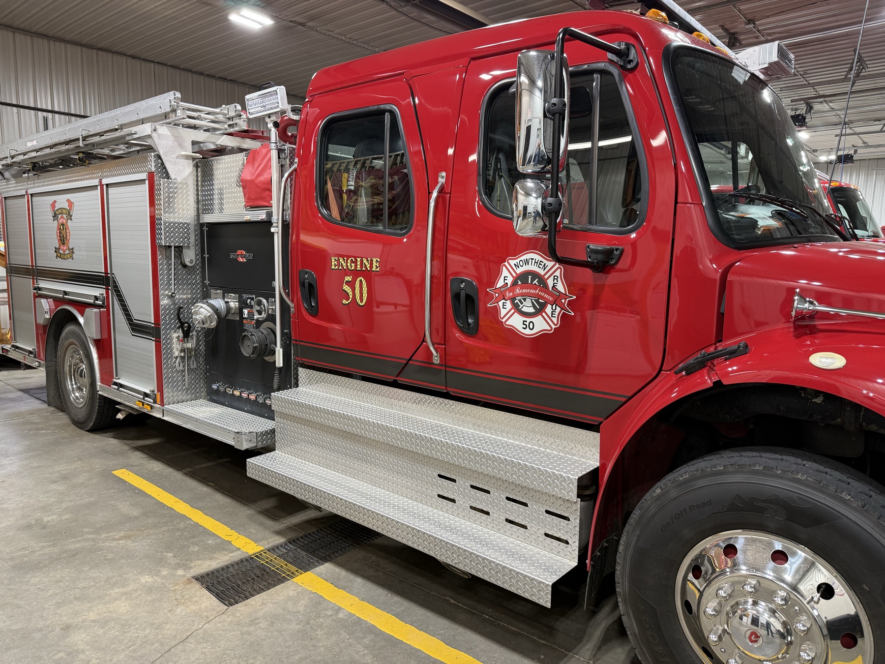 Driver’s side with the pump panel and ladder rack. The door crest reads “In Remembrance, 50.”