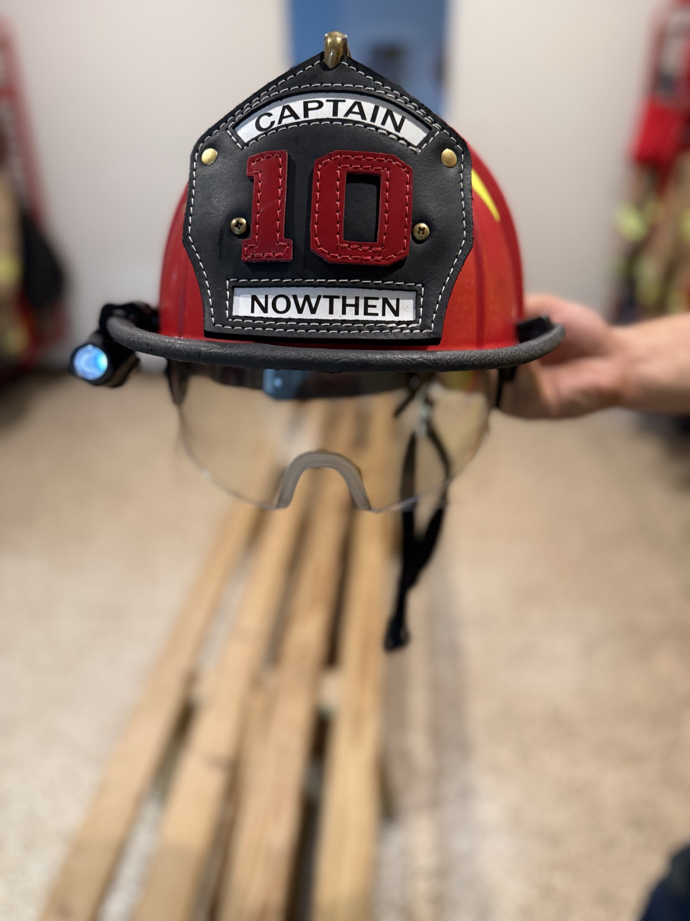 A captain’s helmet: traditional red lid with a leather front shield, clip-on brim light, and flip-down eye protection.